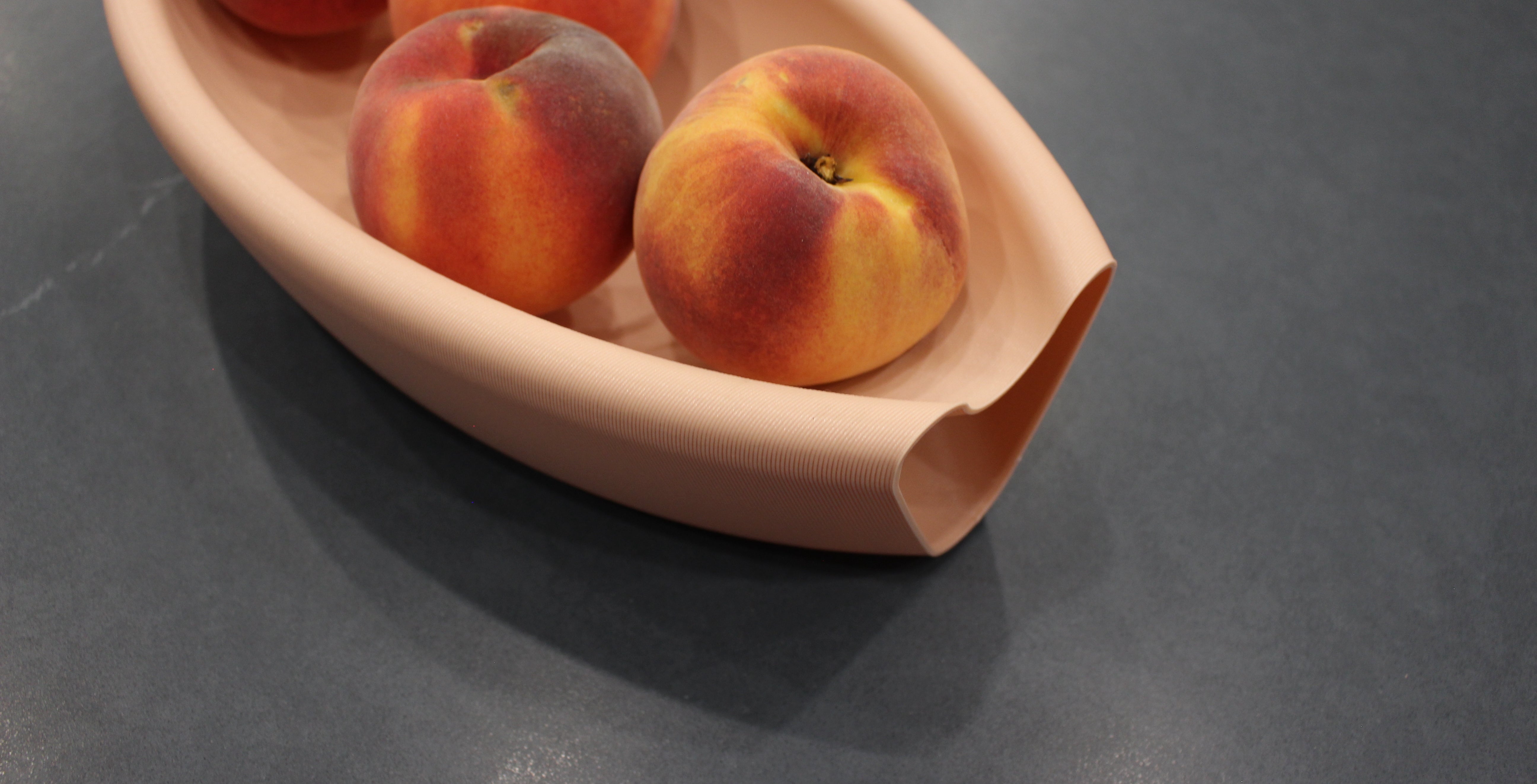3D printed Aera bowl made with recycled plastic by Deme Design, pictured with peaches on a dark marble counter